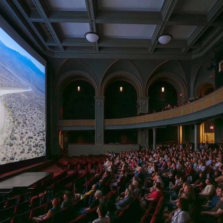 A photo of attendees seated in the Museum’s Kaufmann Theater. The lights are dimmed, and a film is being screened on the large screen.
